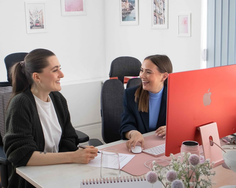 Zwei lachende Kolleginnen an einem Schreibtisch im Büro von Kulturwerke Deutschland