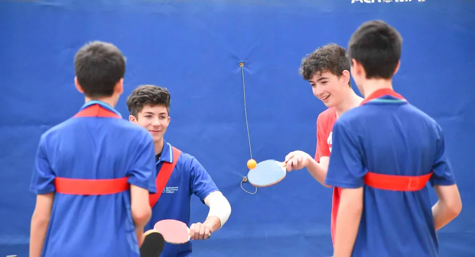 Studenti del Springbank Secondary College giocano a tennistavolo davanti a uno sfondo blu.