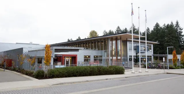 Das moderne Gebäude der École Au-coeur-de-l'île mit amerikanischer Flagge im Vordergrund und Bäumen im Hintergrund.