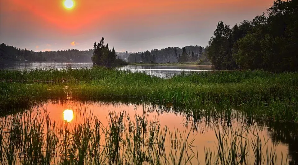 Un lago calmo con fitte foreste verdi e un cielo arancione si riflette nel terreno della John Rennie High School.