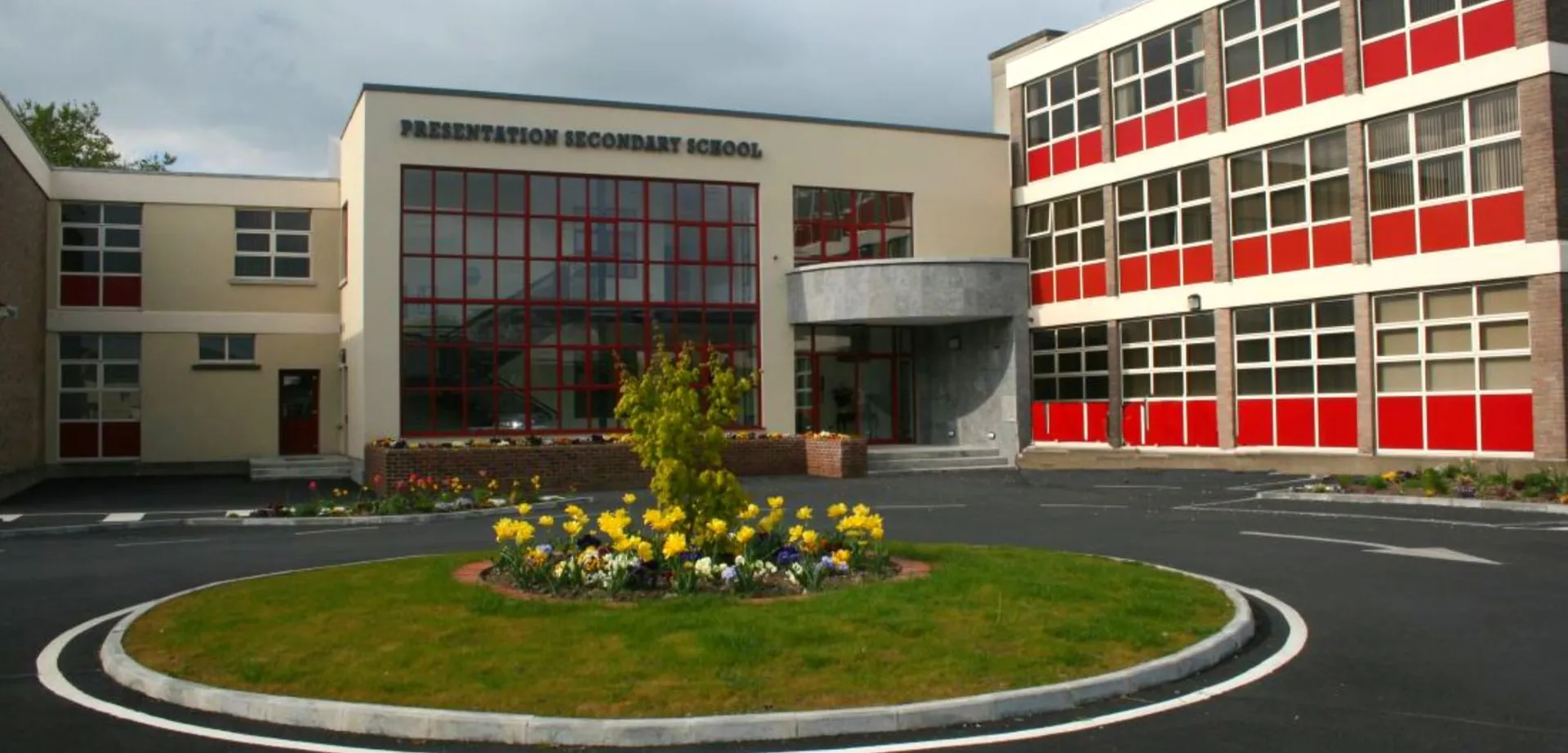 L'edificio principale moderno della Presentation Secondary School Thurles con grandi finestre e un'aiuola circolare in primo piano.