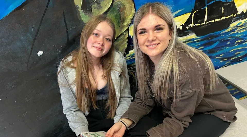 Due studentesse della Haliburton Highlands School posano davanti a un murale astratto e colorato.