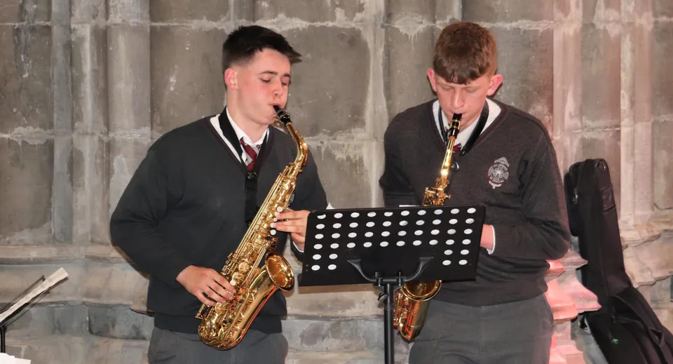 Due studenti della Christian Brothers School Kilkenny suonano il sassofono su un palco davanti a una parete in pietra.