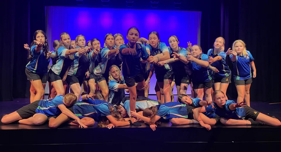 Alcune studentesse della Hervey Bay State High School eseguono una coreografia su un palco con sfondo blu.
