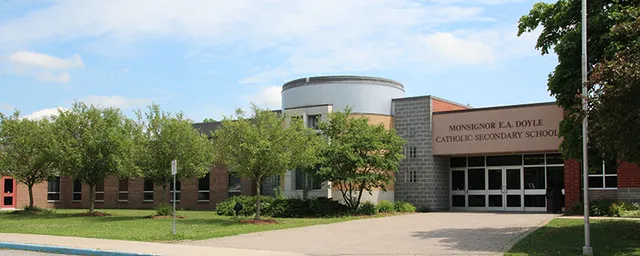 Das moderne Schulgebäude der Monsignor Doyle Catholic Secondary School mit rundem Bauteil steht umgeben von gepflegtem Rasen und grüner Landschaft.