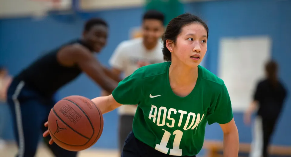 Una studentessa dell'Oxford International College palleggia con un pallone da basket sul campo con altri due giocatori sullo sfondo.