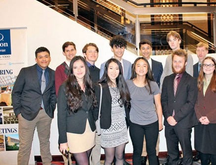 Grupo de jóvenes vestidos con ropa formal posando juntos frente a unas escaleras interiores