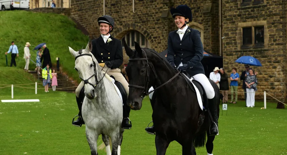 Due cavalieri in abito formale si trovano su un prato davanti a un edificio in mattoni all'interno del campus dell'Ampleforth College.