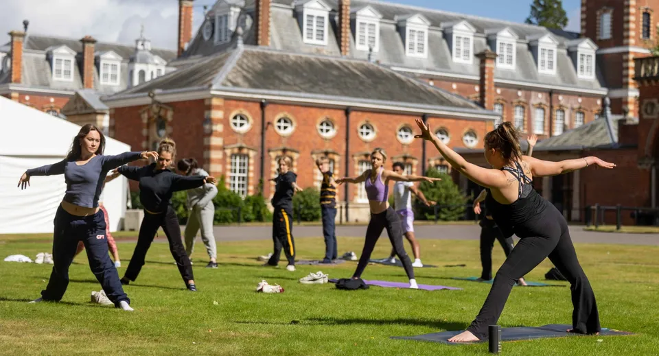 Studenti del Wellington College praticano yoga sul prato davanti a uno storico edificio in mattoni.