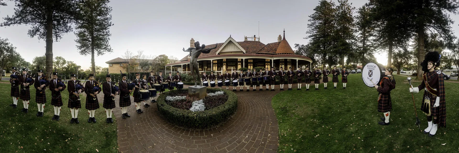 Un gruppo di studenti in abiti formali si trova sul viale davanti all'edificio principale in stile vittoriano del Scotch College.
