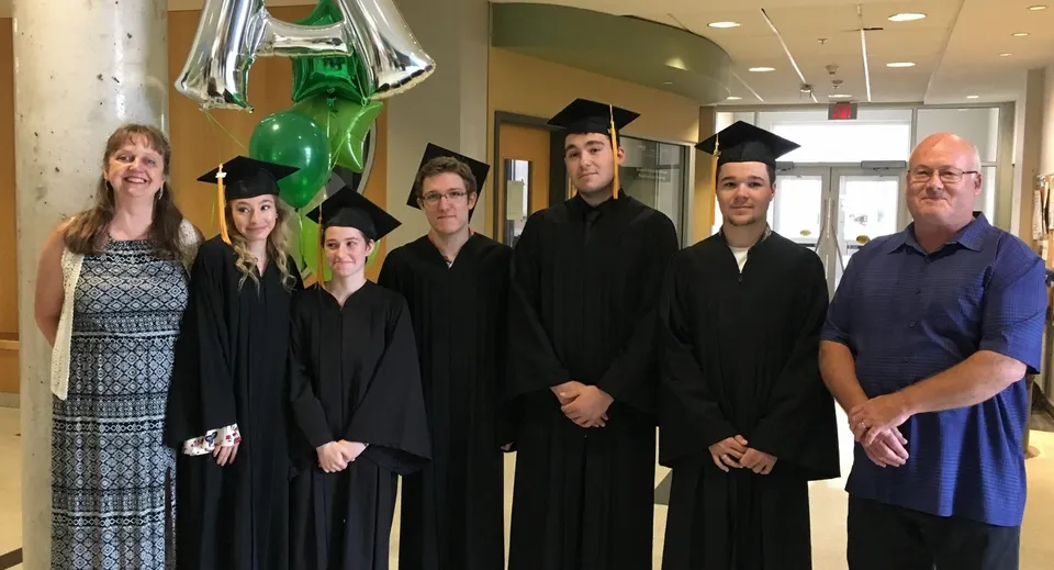 Un gruppo di studenti della A.Y. Jackson Secondary School posa in toga e tocco da diploma nel corridoio decorato con palloncini.