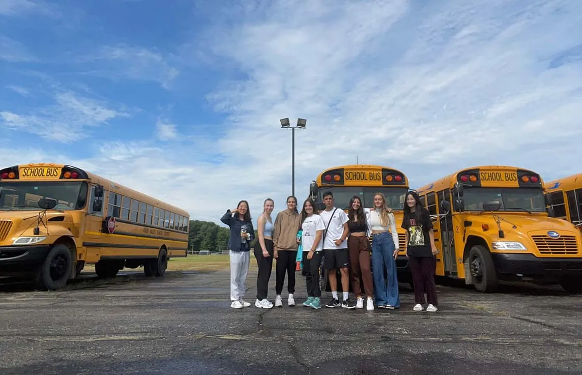 Ocho jóvenes ante autobuses escolares amarillos en un aparcamiento de Michigan