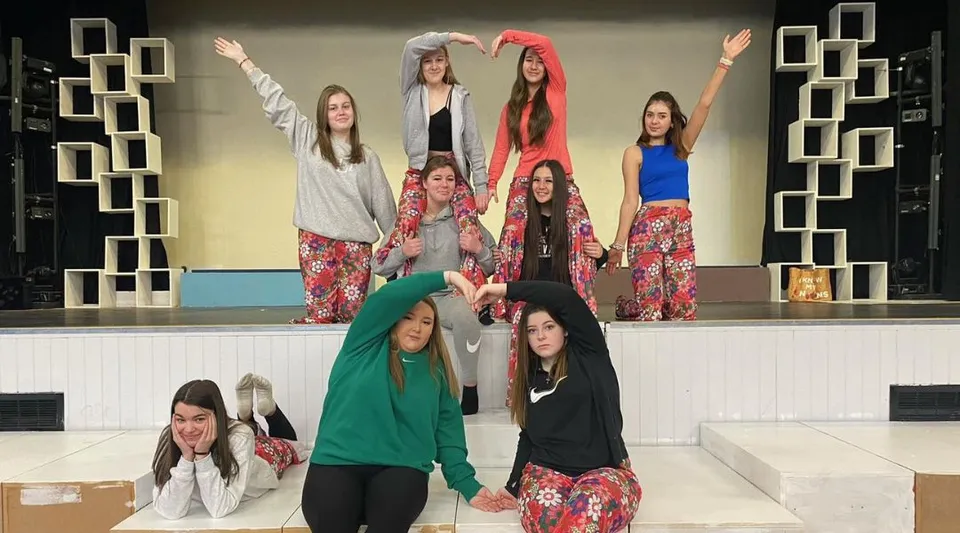 Un gruppo di giovani studentesse dell'Our Lady Catholic College è su un palco in abiti colorati con uno sfondo geometrico.