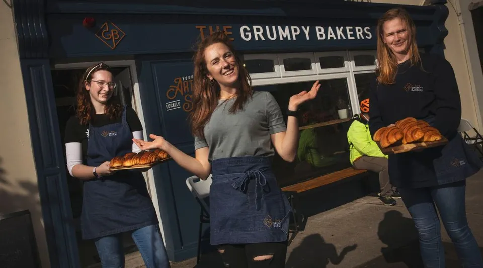 Tre studentesse del St. Colman’s Community College sono davanti al negozio The Grumpy Bakers tenendo in mano prodotti appena sfornati.