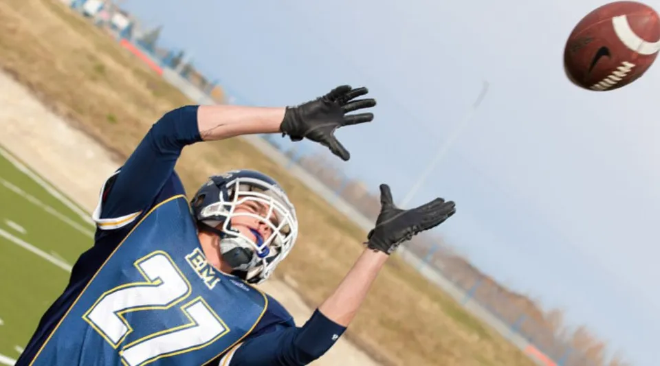 Un giocatore di football in divisa blu scuro prende un pallone da football sul campo sportivo della Queen Elizabeth School.