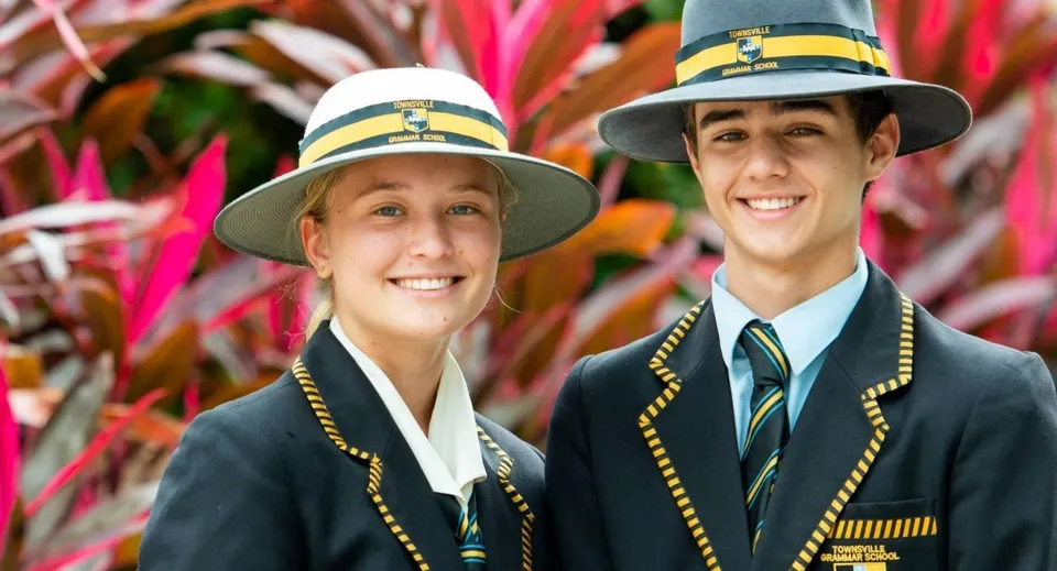 Due studenti della Townsville Grammar School indossano cappelli tradizionali e divise davanti a uno sfondo colorato.
