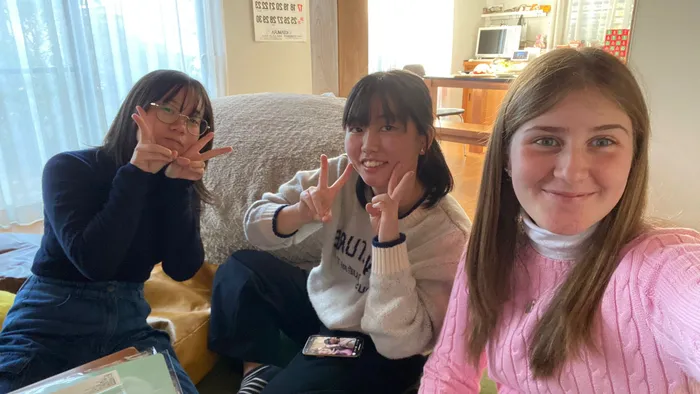 Tre ragazze sedute in soggiorno sorridono facendo il segno della pace