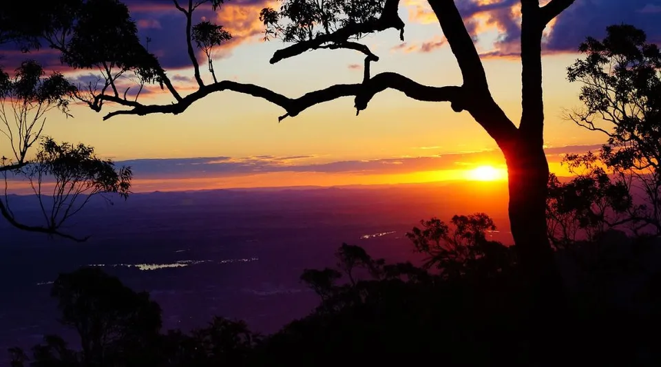 Un tramonto su un paesaggio montuoso con alberi in primo piano nel terreno della Kingaroy State High School.
