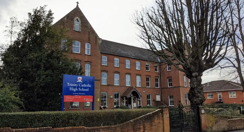 L'edificio in mattoni con una torretta nel campus della Trinity Catholic High School è circondato da alberi e da una recinzione.