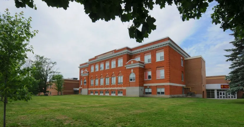 Il grande edificio in mattoni della Carleton Place High School sorge su un prato circondato da alberi verdi.