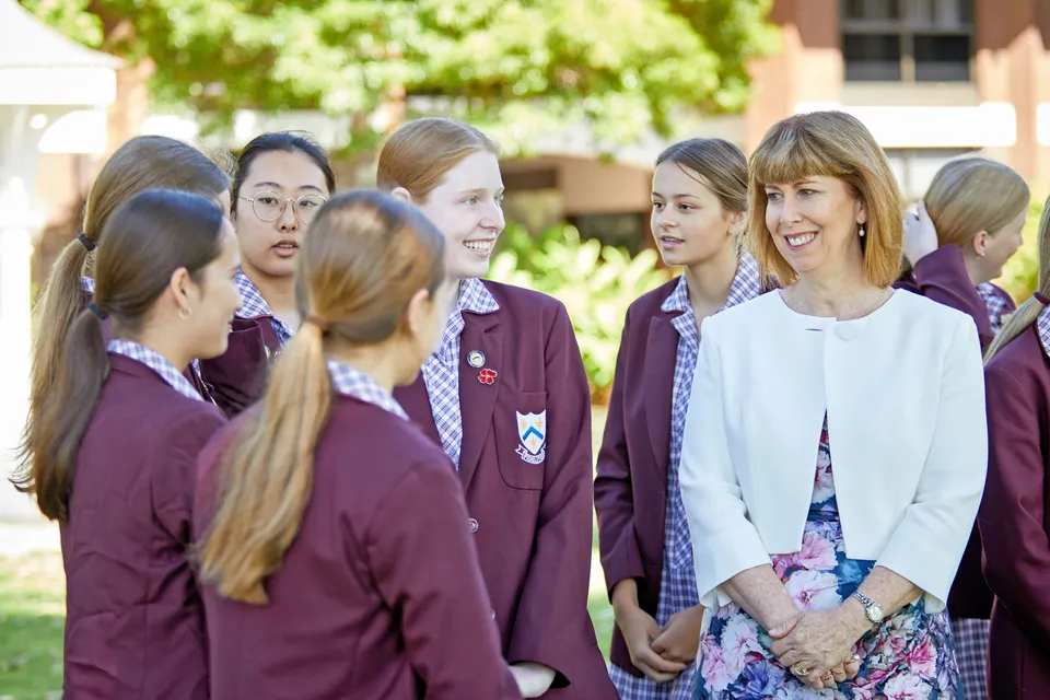 Un gruppo di giovani studentesse si trova nel campus della St. Mary's Anglican Girls' School davanti ad alberi ed edifici scolastici.