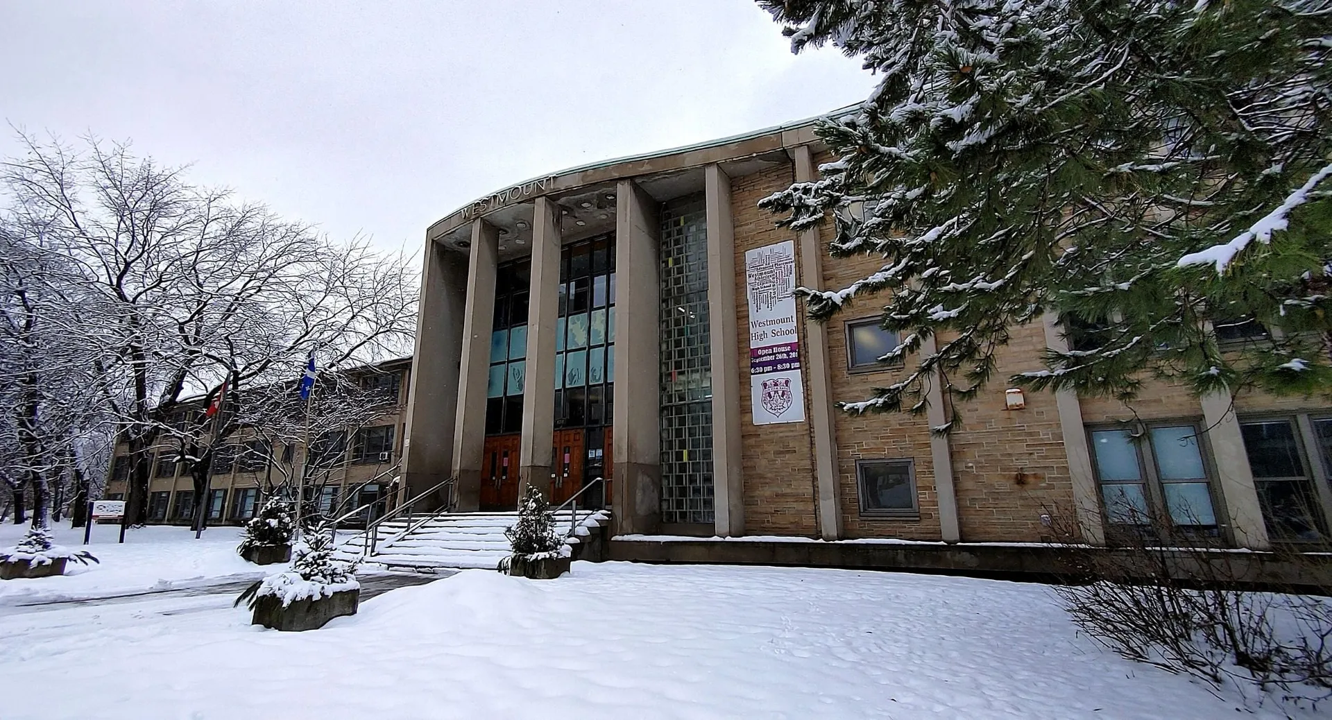 Il terreno innevato con l'imponente edificio in pietra della Westmount High School in inverno con alberi spogli.
