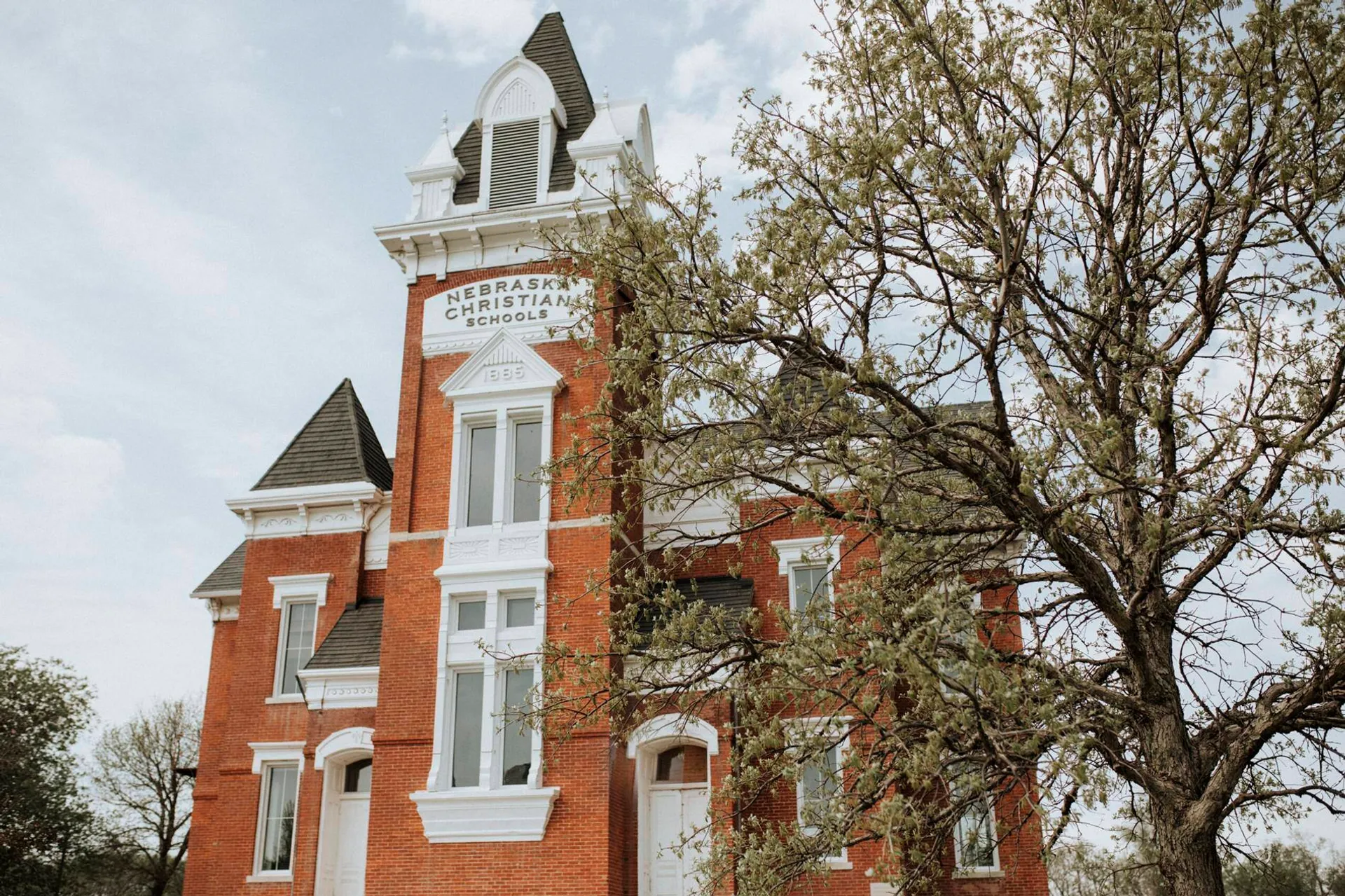 L'edificio storico in mattoni con un'alta torre dell'orologio nel campus della Nebraska Christian Schools è circondato da alberi spogli.
