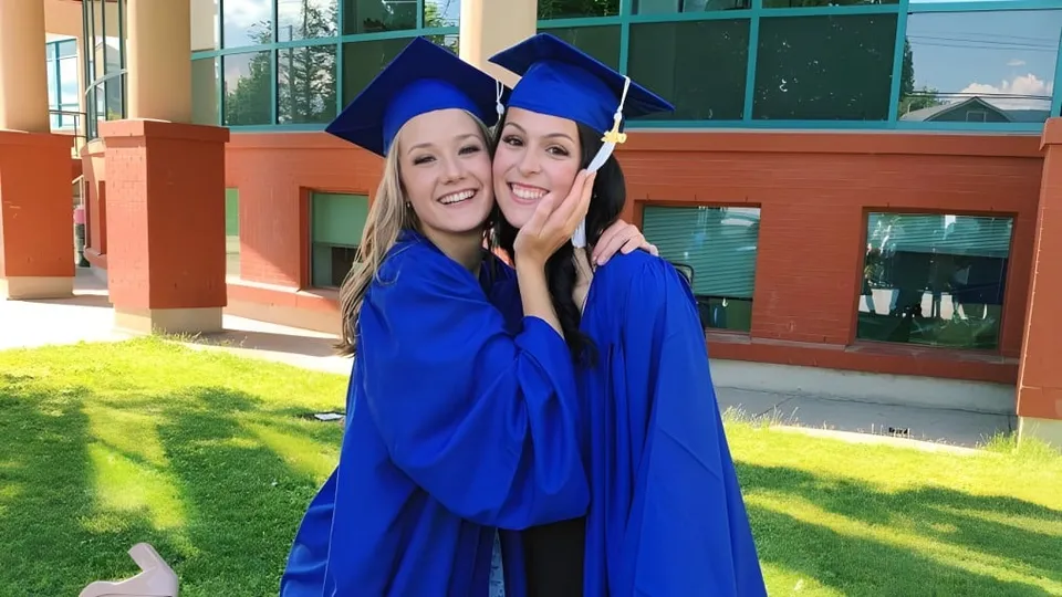 Due studentesse sorridenti in toga blu da diploma sono in piedi davanti all'edificio scolastico della W. L. Seaton Secondary School.