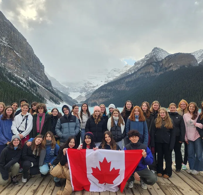 Gran grupo de estudiantes con una bandera de Canadá ante un lago de montaña nevado
