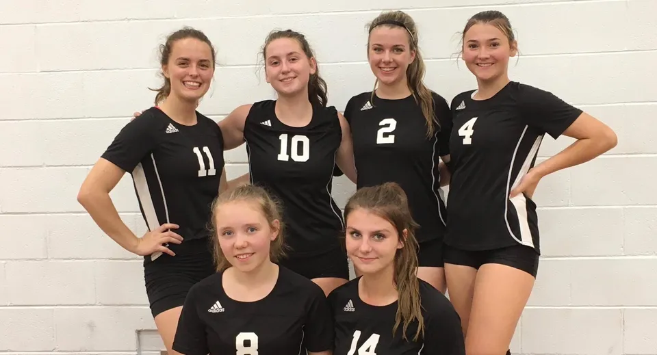 Sei studentesse della Salmo Secondary School posano insieme in divise nere da pallavolo davanti a una parete bianca.