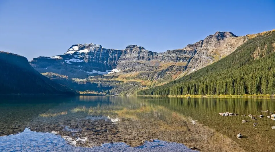 Un lago limpido riflette le montagne rocciose e i boschi nella regione della Thorsby Junior Senior High School.
