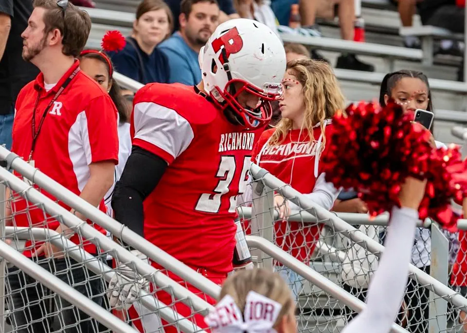Studenti della Richmond High School indossano uniformi sportive rosse e bianche e si trovano su una tribuna dietro una ringhiera metallica.