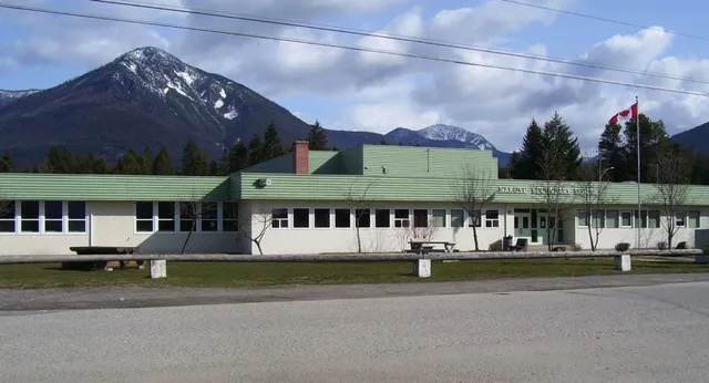El moderno edificio de varias plantas de la Nakusp Secondary School con tejado verde ante montañas y árboles.