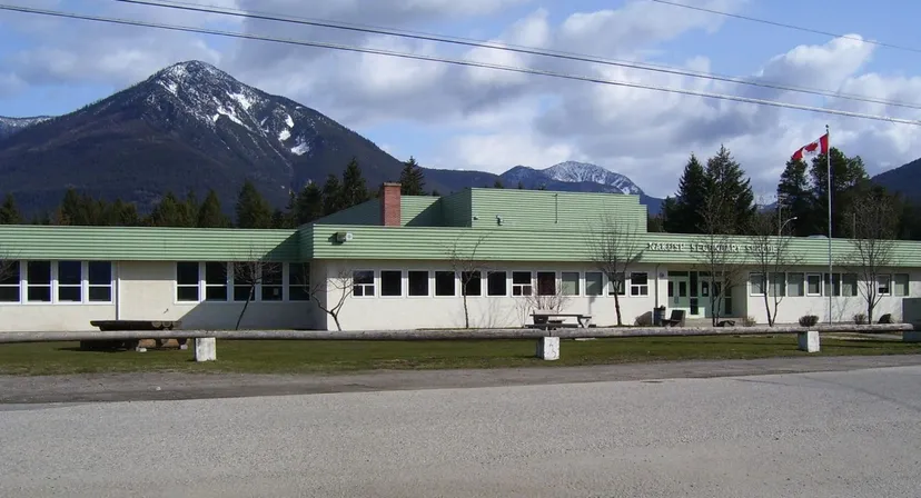 L'edificio moderno a più piani della Nakusp Secondary School con tetto verde davanti a montagne e alberi.