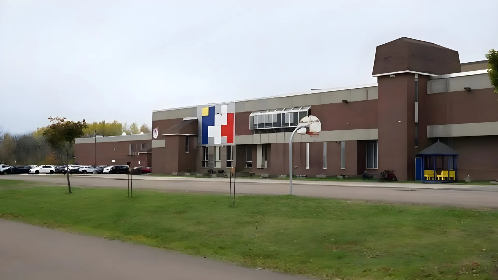 L'edificio moderno a più piani della École Mathieu-Martin sorge su un prato con un canestro da basket in primo piano.