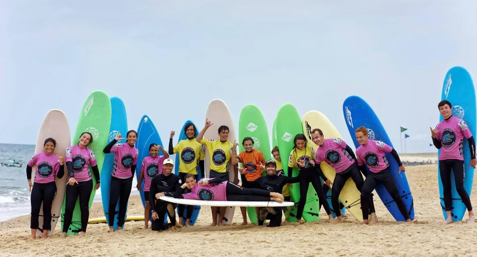 Studenti del Bosworth Independent College si trovano sulla spiaggia davanti all'oceano con mute colorate e tavole da surf.