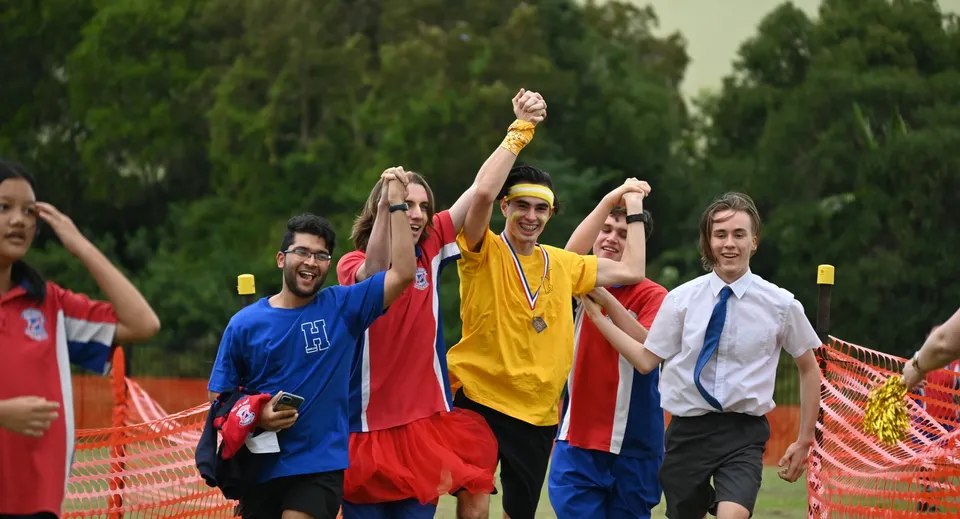Un gruppo di studenti festanti alza le braccia nel parco del campus della Aspley State High School.