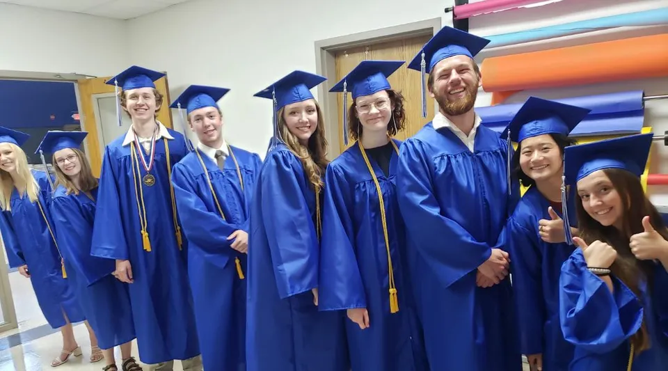 Un gruppo di diplomati della Cambridge Christian School è in posa nel corridoio in toga e tocco blu per una foto di gruppo.
