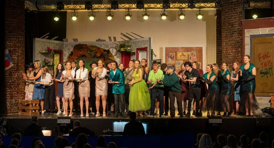 Un gruppo di studenti della Panorama Ridge Secondary School si trova in abito formale su un palco davanti a una parete di mattoni.