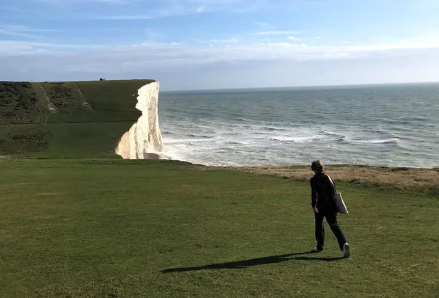 Persona paseando por una pradera sobre los acantilados blancos de la costa inglesa