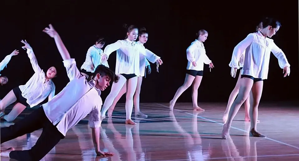 Un gruppo di studenti della Rancho Solano Preparatory School balla su un palco al buio con costumi leggeri e fluenti.