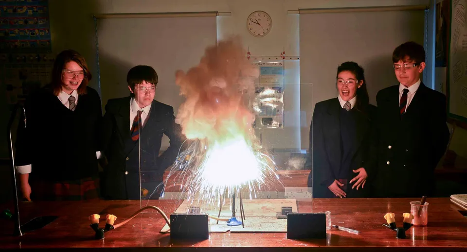 Studenti della Fyling Hall School eseguono un esperimento con piccoli fuochi d'artificio a un tavolo.