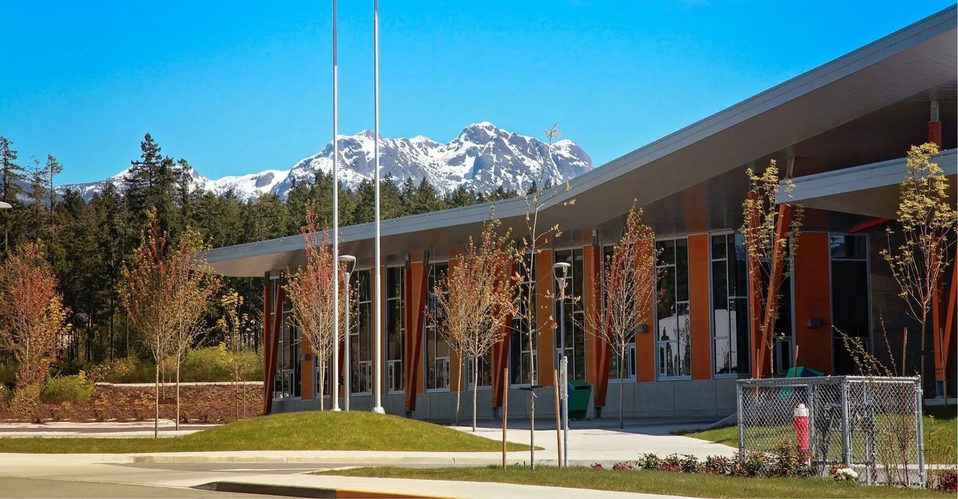 L'edificio moderno della Alberni District Secondary School con grandi finestre e un prato in primo piano davanti a montagne innevate.