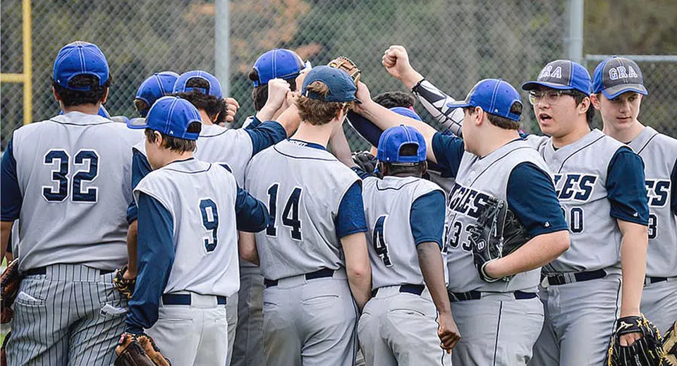 Studenti della Grand River Academy festeggiano insieme sul campo da baseball con i compagni di squadra sullo sfondo.