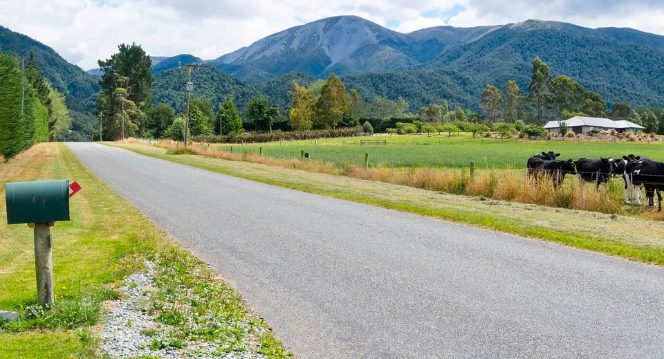 Una strada sterrata tortuosa attraversa un prato verde con vista su montagne innevate e fitti boschi all'interno della proprietà del Mount Hutt College.