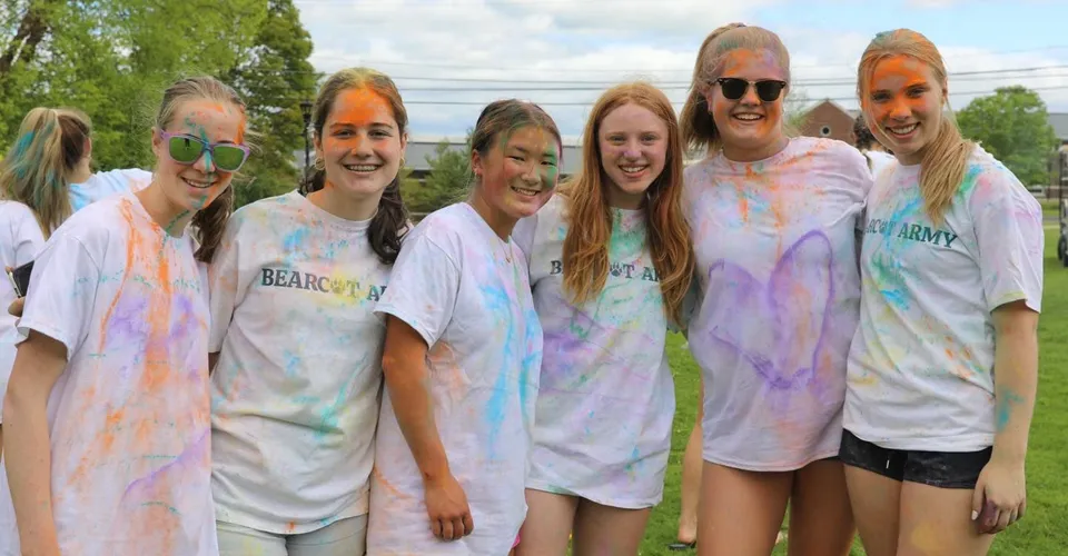 Un gruppo di studenti della Hotchkiss School posa all'aperto coperto di colore vivace davanti a uno sfondo verde.