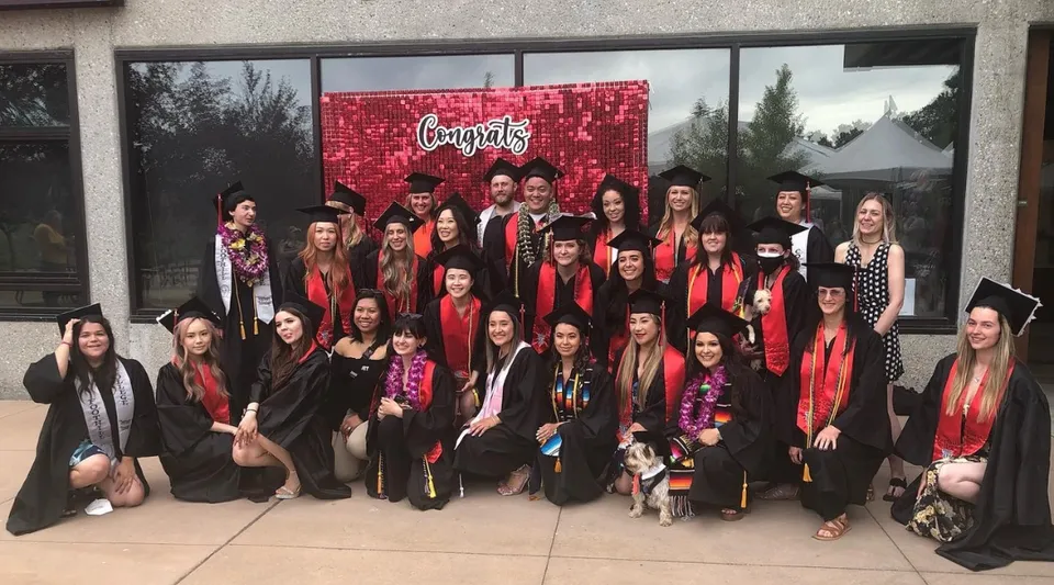 Un grande gruppo composto prevalentemente da giovani donne sta in piedi davanti a uno sfondo rosso del Foothill College con la scritta 'Congrats'.
