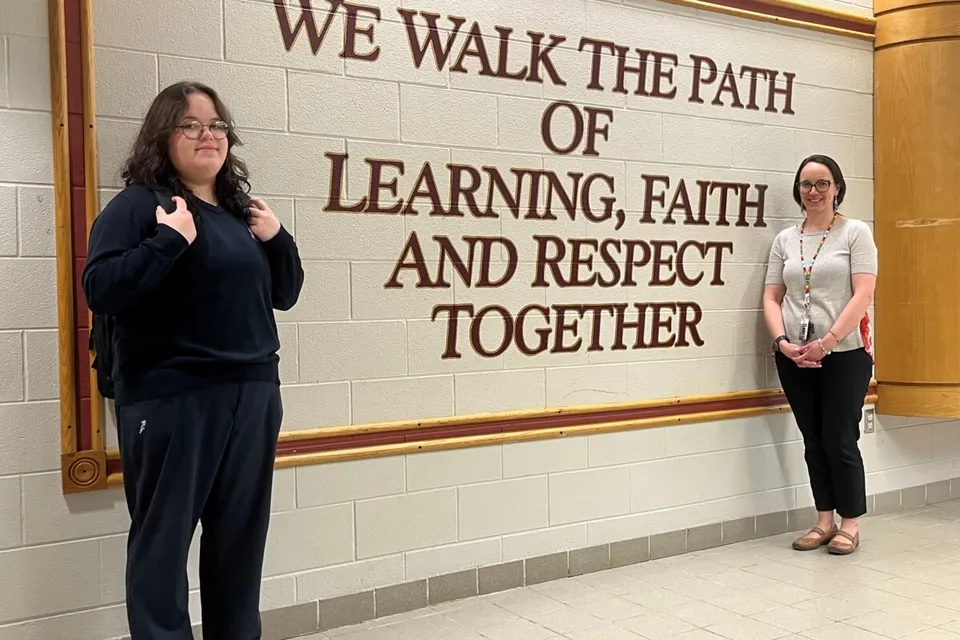 Una studentessa e una donna stanno nel corridoio della Monsignor Doyle Catholic Secondary School davanti a una parete scritta.