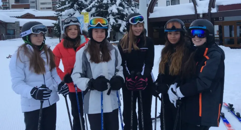Un gruppo di studentesse della Caterham School si trova nell'area esterna innevata davanti agli edifici in abbigliamento invernale, con maschere da sci e guanti.