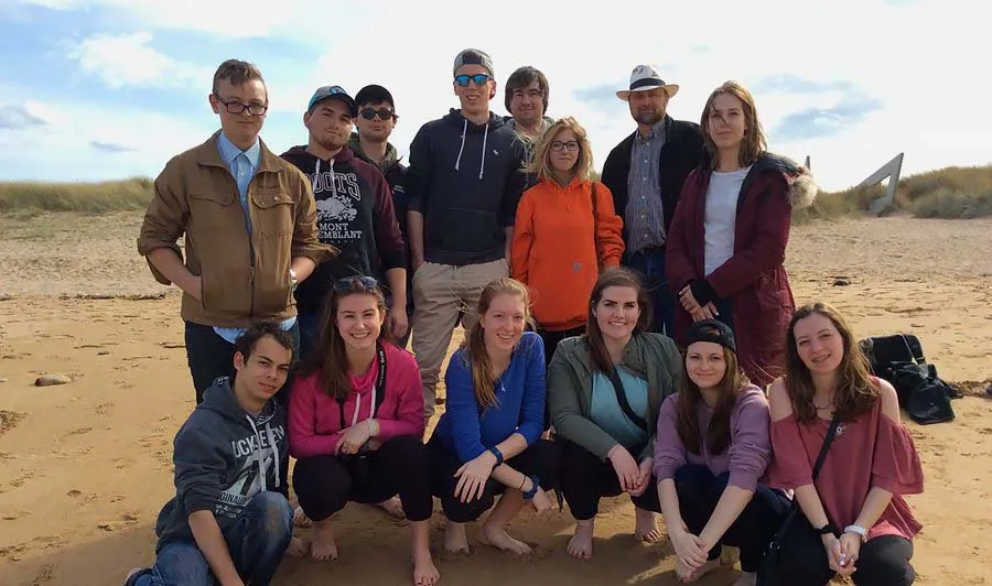 Un grupo de estudiantes de la Blenheim District High School está junto en una playa de arena bajo un cielo nublado.